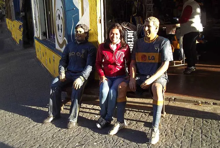 Girl wearing red coat sitting between two soccer players' statues.