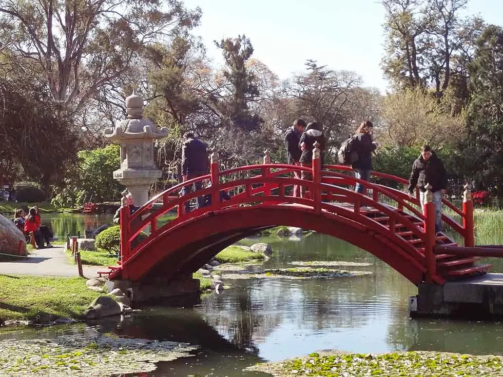 People walking over a red bridge in the Japanese Garden in Buenos Aires.