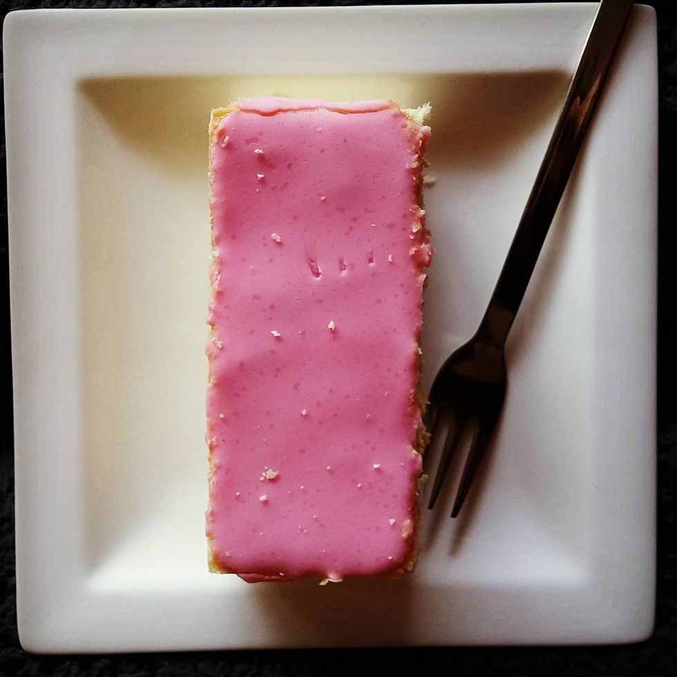 Pink tompouce on a white plate and a tiny silver fork in Amsterdam.