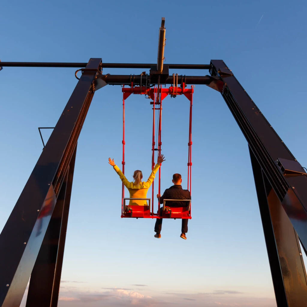 Young couple swing over the edge of Adam Tower