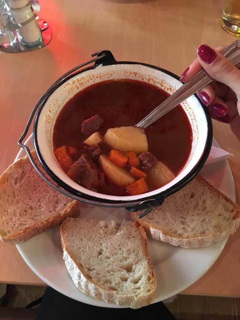 Woman's hand holding spoon in a Goulash soup surrounded by bread in Budapest