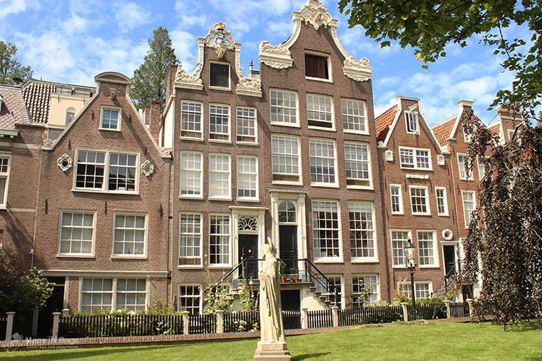 Amsterdam's houses around a white statue and green grass at the begijnhof.