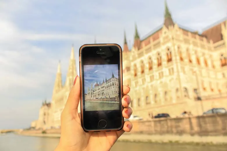 Hand holding Iphone with image of the Hungarian Parliament in front of the Hungarian Parliament