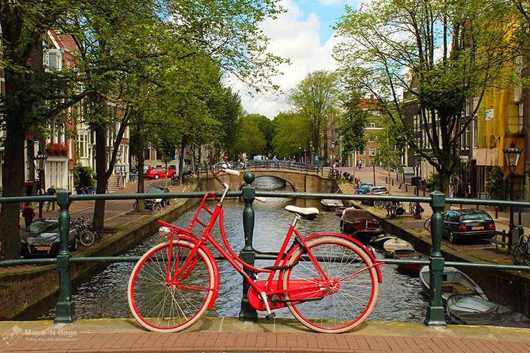 Red bike attached to a bridge over a canal in Amsterdam.
