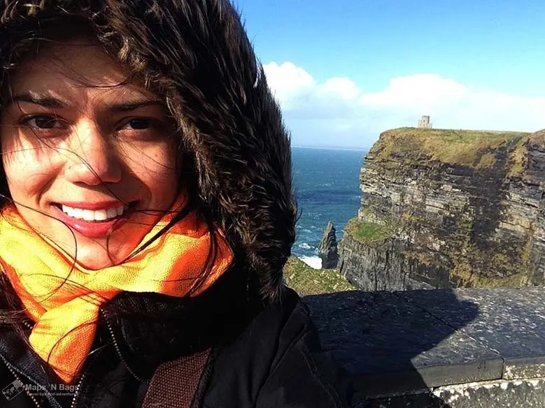 Girl wearing a hoodie and smiling at the camera at the Cliffs of Moher #Ireland #CliffsofMoher #Europe #Travel