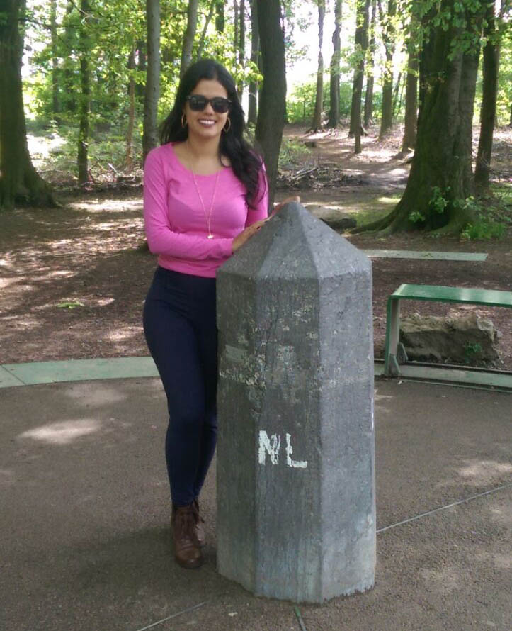 Women wearing a pink blouse and black sunglasses standing next to a stack in the Three country point on the German, Belgian, and Dutch border.