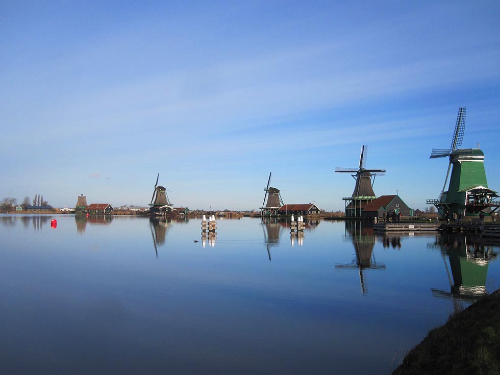 Windmills next to a lake reflecting the blue sky in Zaanse Schans.