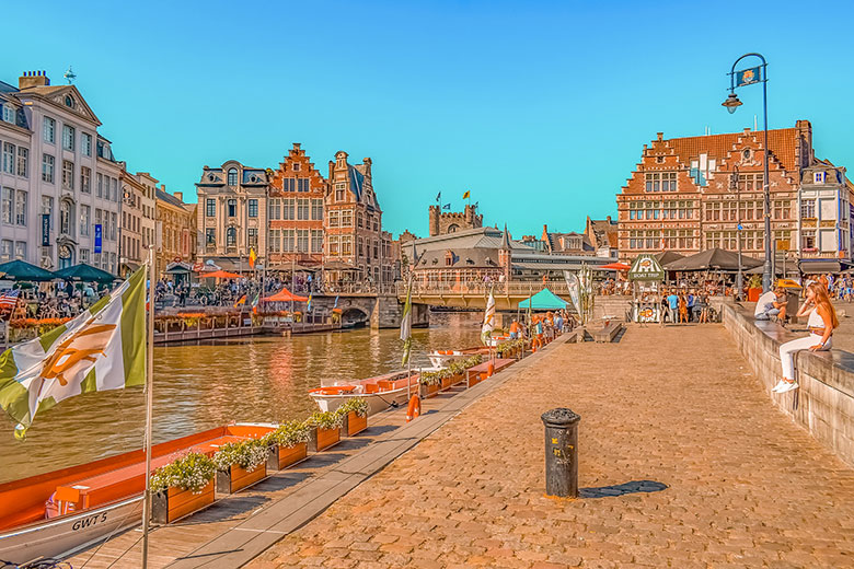 Canal in Ghent, Belgium, near decorated sidewalk with flowers and medieval houses.