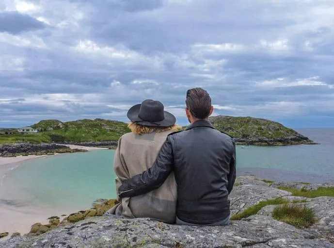 Couple sitting Achmelvich Beach in Scotland NC 500, a unique travel destination