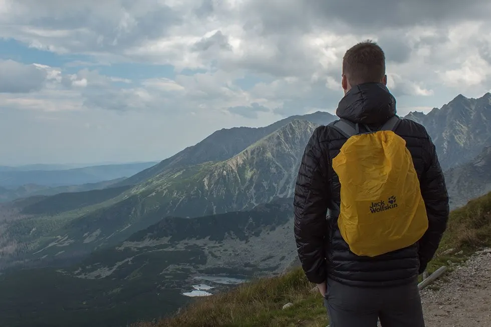 Man wearing a black jacket and a yellow backpack looking over the Tatra Mountains in Poland