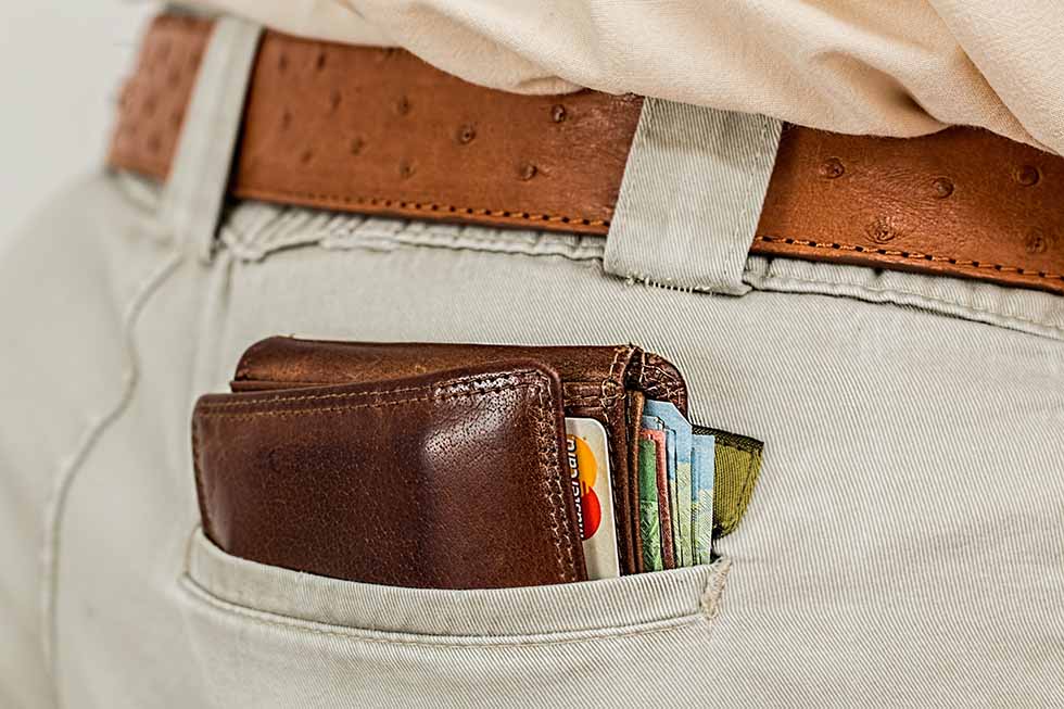 Brown leather wallet with cards and money in the back pocket of a male pair of paints. #Travel #Scams