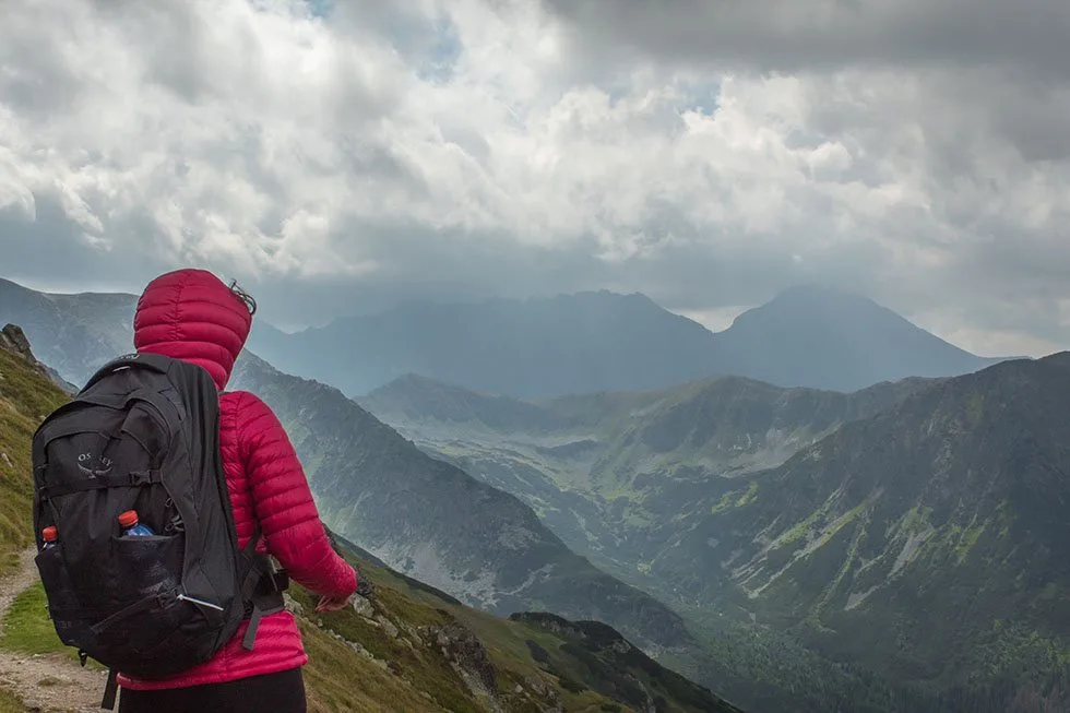 Woman wearing pink jacket and wearing a backpack on top of the Tatra mountains in Poland and Slovakia