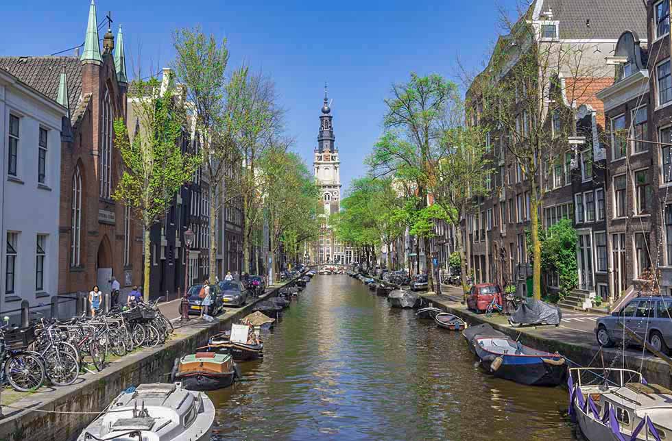 Houses and boats on both sides of a canal and the Zuiderkerk's tower in Amsterdam.
