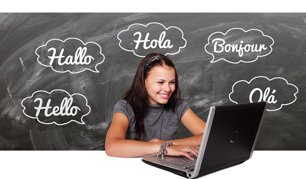 Brunette smiling while sitting in front of a black laptop and surrounded by Spanish words