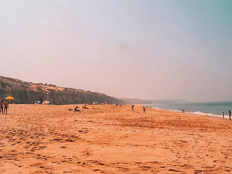 People on Meco beach near Lisbon in front of a cliff enjoying the sun.