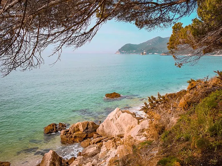 Blue sea water, trees, and rocks at Galapos Beach near Lisbon, Portugal.