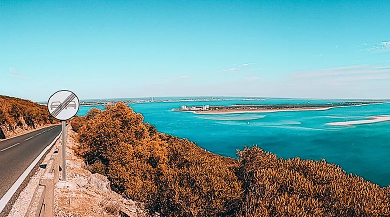 Road on a hill covered with trees overlooking the blue Atlantic sea and Troia peninsula.