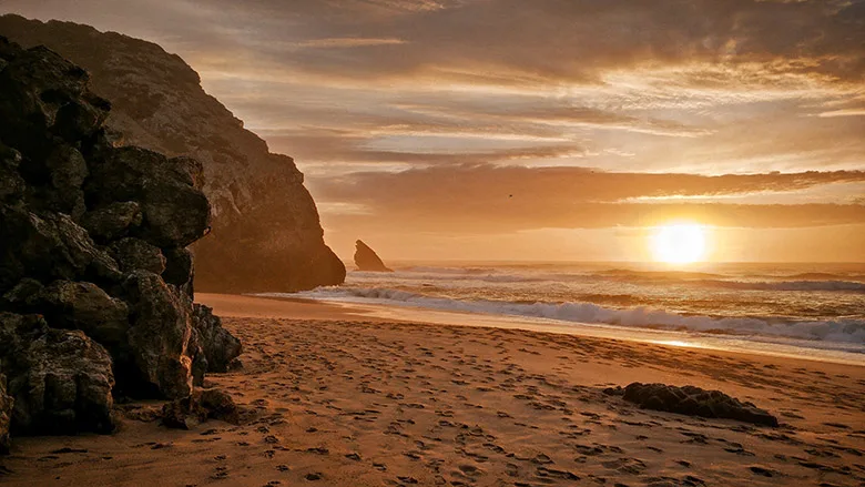 Sand, rocks and sea at a sunset at Adraga Beach in Lisbon, Portugal.