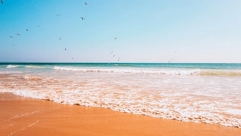 Orange sand and blue water in a sunny day at Praia da Mata in Lisbon, Portugal