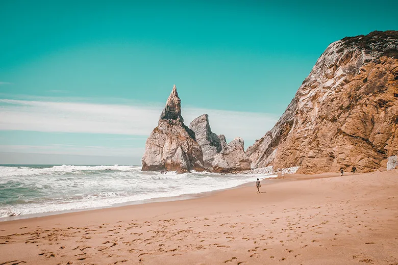 Person walking on the sand near rocks at Ursa beach in Lisbon, Portugal