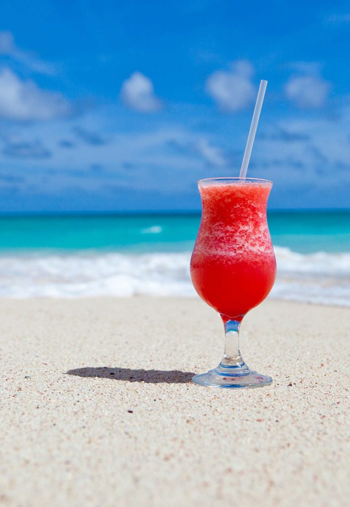 Red drink on the white sand in front of the blue sea