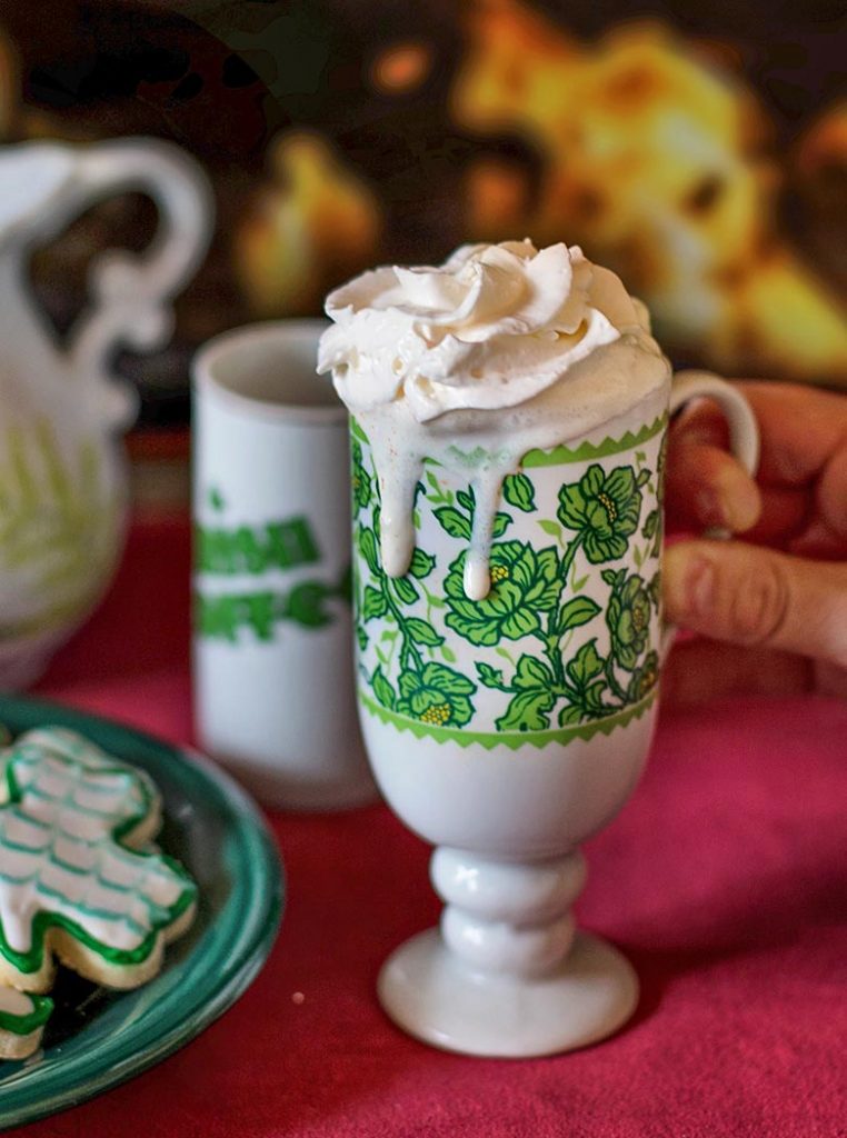 Whipped cream falling over the edge of a green Irish mug filled with coffee