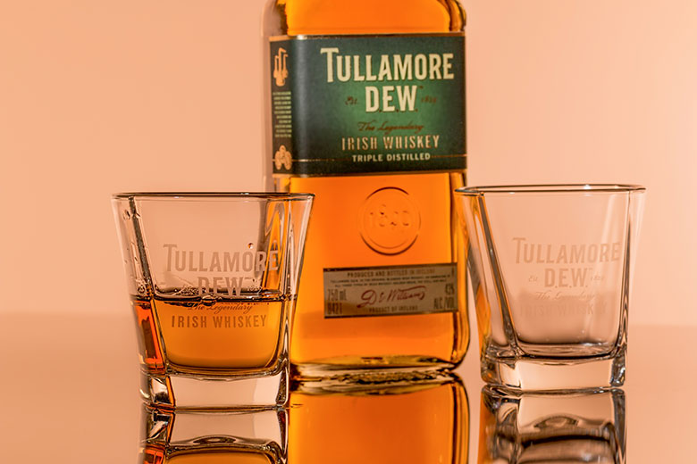 Bottle of the Irish whiskey Tullamore near two glasses, one half filled and the other empty