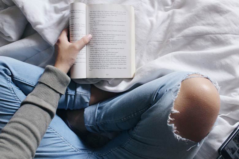 Woman with thorn pants reading a book on bed