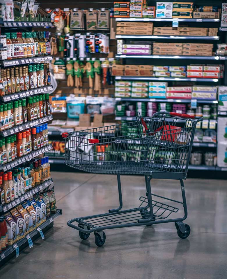 Supermarket cart next to shelves. Tips on how to save money for travel.